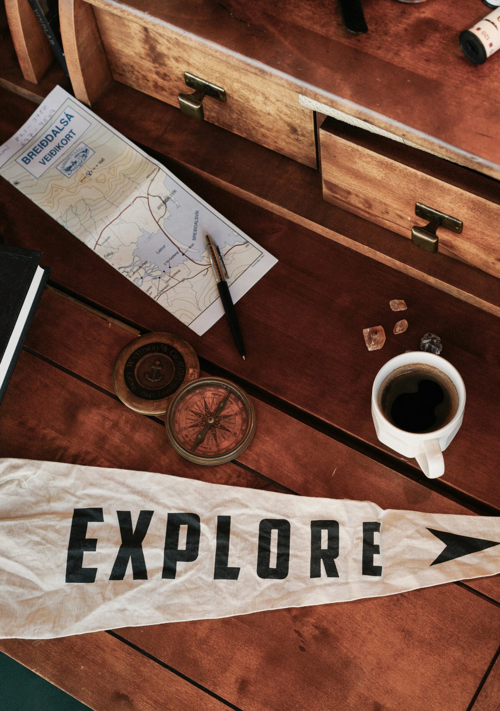 A flat lay of travel essentials: map, compass, pen, and coffee for an adventure.